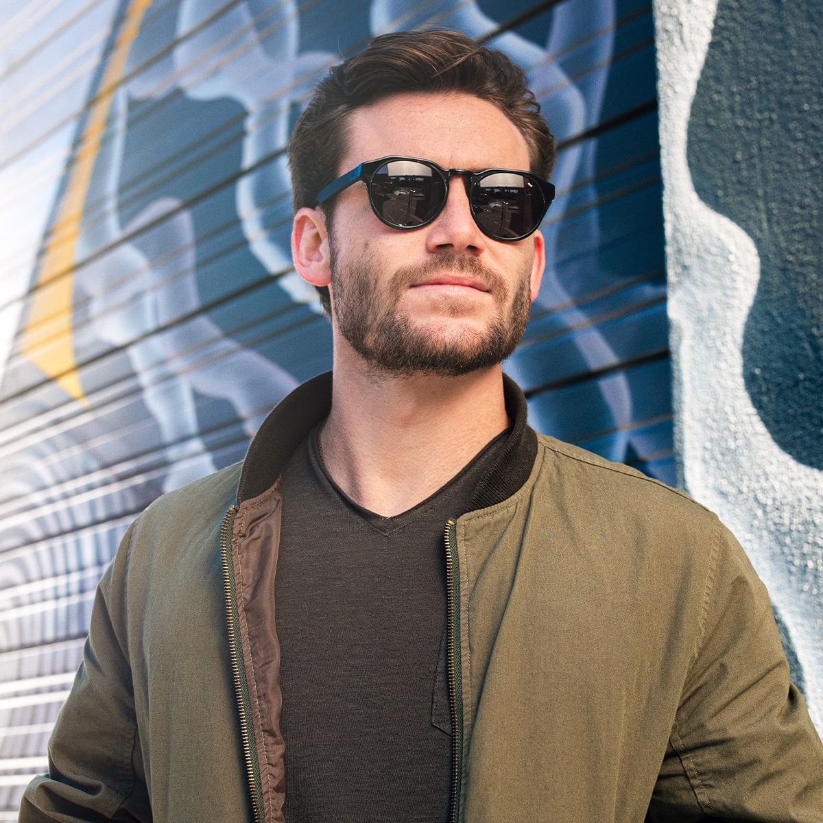 bearded man wearing distil cooper sunglasses, green bomber jacket